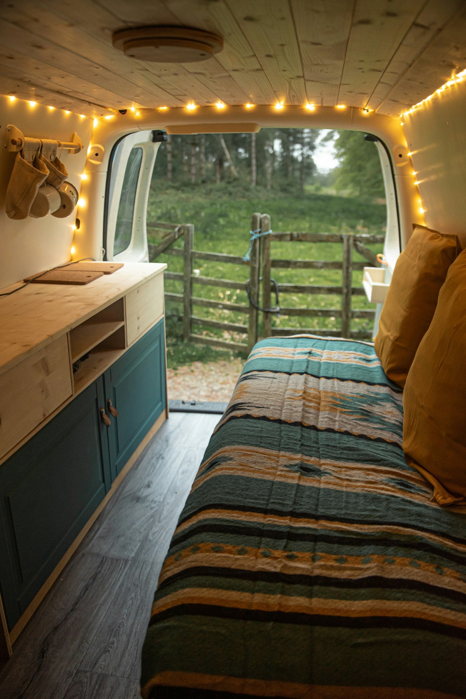 Converted van interior with a bed and a side window looking onto a field